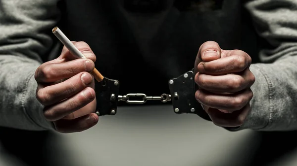 手錠を掛けられてタバコを吸って逮捕された麻薬中毒者 暗い黒い背景に中毒に苦しんでいる灰色のスエット シャツ — ストック写真