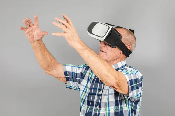 Abuelo mira en gafas VR, gestos de mano, en una espalda gris — Foto de Stock