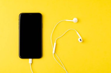 Sarı arka planda kulaklıklı akıllı telefon. t'den görünüm