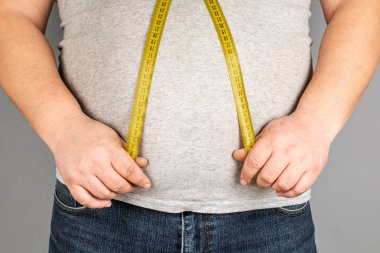 Bir adam bir ölçüm bandı ile onun yağ göbek ölçer. gri bir ba üzerinde