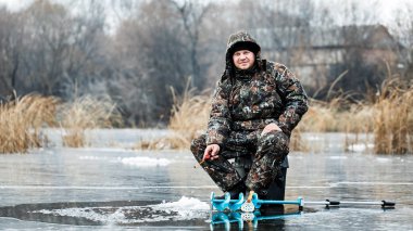 Genç bir adam bir delikten buzda balık tutuyor. Balık tutma kış