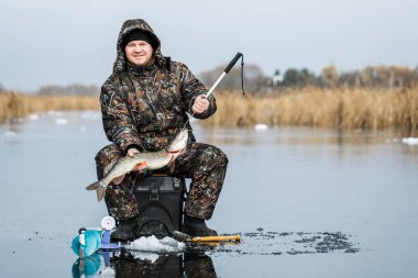 Genç bir adam bir delikten buzda balık tutuyor. Balık tutma kış