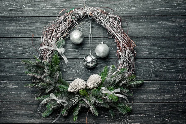Christmas wreath with ornaments on black wooden background.