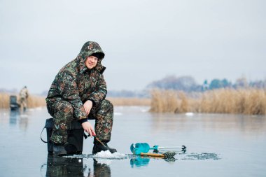 Genç bir adam bir delikten buzda balık tutuyor. Balık tutma kış