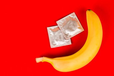 Prezervatif ve muz, güvenli seks. Seks oyuncak. Kırmızı arka planda.