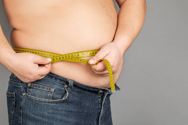 Мужчина измеряет свой живот измерительной лентой. на скамье подсудимых
