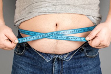 Bir adam bir ölçüm bandı ile onun yağ göbek ölçer. gri bir ba üzerinde