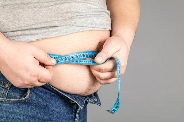 Um homem mede a barriga gorda com uma fita métrica. em uma ba cinza — Fotografia de Stock
