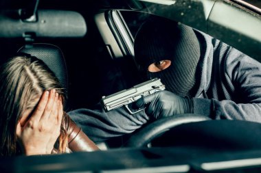 Silahlı maskeli bir soyguncu arabadaki bir kadını tehdit ediyor. Soyguncu