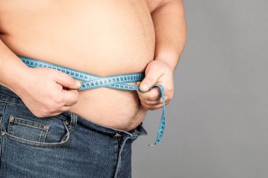 Bir adam bir ölçüm bandı ile onun yağ göbek ölçer. gri bir ba üzerinde