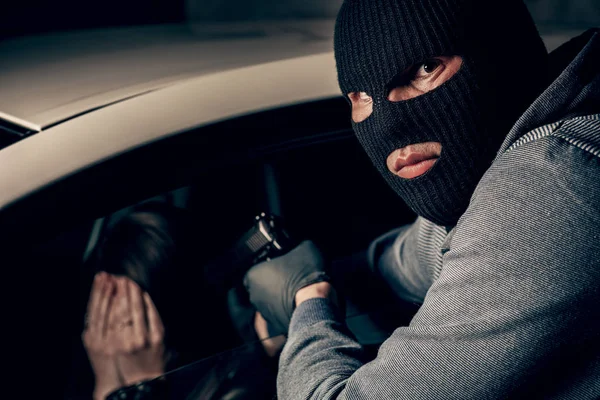 Грабитель в маске с пистолетом угрожает женщине в машине. грабитель — стоковое фото