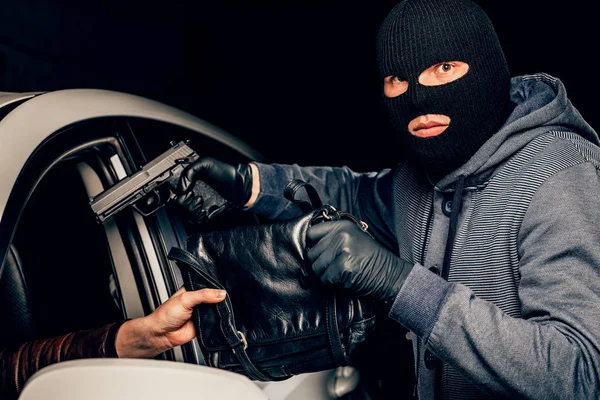 En maskerad rånare med en pistol hotar en kvinna i en bil. Rånare — Stockfoto