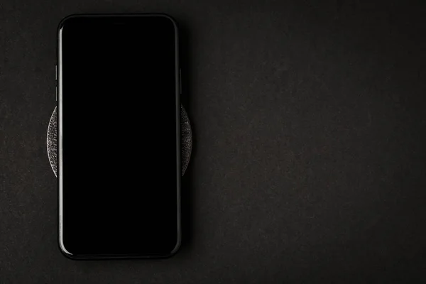 Smartphone is charged by a wireless charger on a black backgroun — Stock Photo, Image