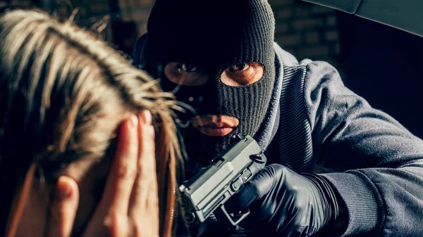Silahlı maskeli bir soyguncu arabadaki bir kadını tehdit ediyor. Soyguncu