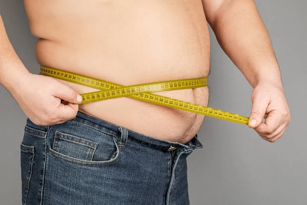 Ein Mann misst seinen dicken Bauch mit einem Maßband. auf einem grauen Ba Stockfoto