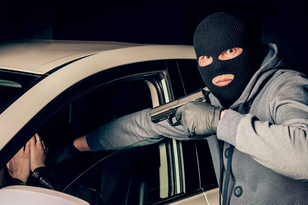En maskerad rånare med en pistol hotar en kvinna i en bil. Rånare — Stockfoto