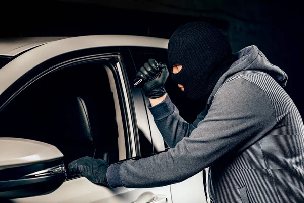 Um ladrão vestido com uma máscara preta, apontando uma lanterna para o dri — Fotografia de Stock