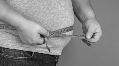 Bir adam bir ölçüm bandı ile onun yağ göbek ölçer. gri bir ba üzerinde