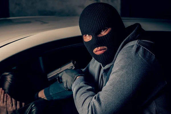 En maskerad rånare med en pistol hotar en kvinna i en bil. Rånare — Stockfoto