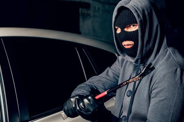 Male thief is going to open the car door with a crowbar. Stock Picture