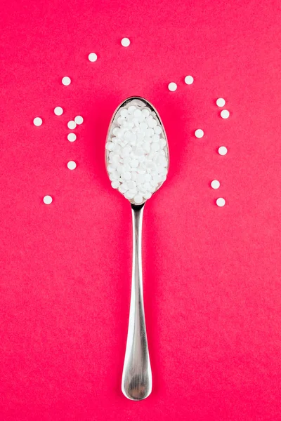 Таблетка для замены сахара с ложкой на красном фоне — стоковое фото