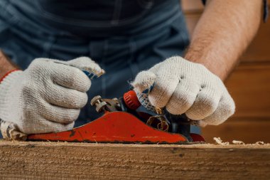 Marangozluk yapan bir marangoz atölyesindeki ahşap bir tahtanın yüzeyinde el uçağıyla uçuyor. Onarım ve inşaat kavramı.