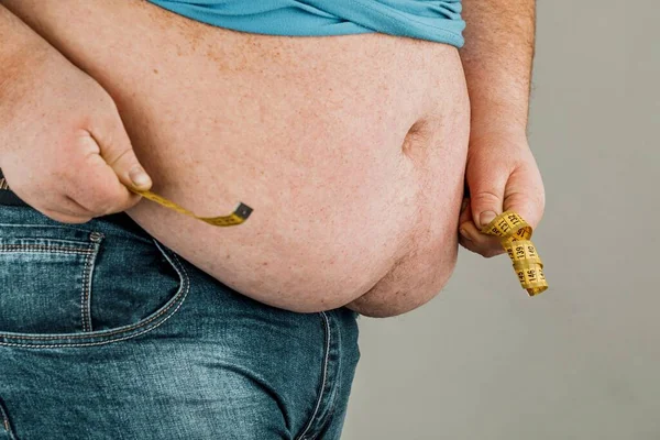 Homem Mede Barriga Gorda Com Uma Fita Métrica Fundo Cinza — Fotografia de Stock