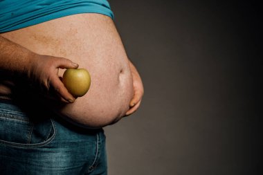 Şişman adam çıplak karnının önünde bir elma tutuyor. Diyet ve sağlıklı yemek kavramı..