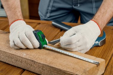 Elinde kalem ve mezura olan bir marangoz masanın üzerindeki tahta tahtayı ölçer..