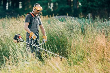Erkek bahçıvan çim biçme makinesiyle çimleri biçiyor..