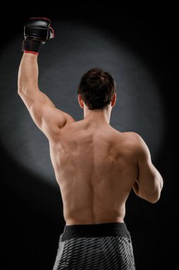 Atletik adam kollarını kaldırdı, sporcunun kaslı vücudu siyah bir arka plana doğru görünüyordu.