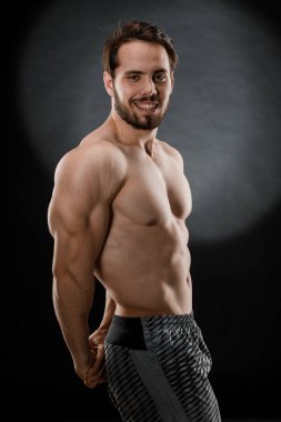 Tişörtsüz yakışıklı kaslı bir adam karanlık bir fotoğraf stüdyosunda fotoğrafçıya poz veriyor. Spor konsepti.
