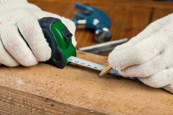 Elinde kalem ve mezura olan bir marangoz masanın üzerindeki tahta tahtayı ölçer..