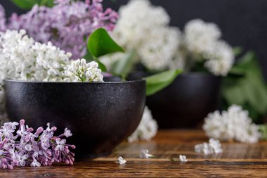 Güzel feolette ve güzel yalan bembeyaz Lila çiçek bardak siyah. Ahşap arka plan üzerinde natürmort. Yakın çekim.