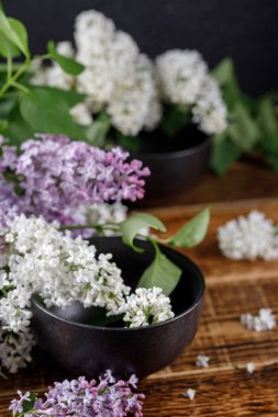 Muhteşem mor ve kar-beyaz leylak çiçeklerle iki siyah seramik bardak. Ahşap arka plan üzerinde natürmort. Yakın çekim.