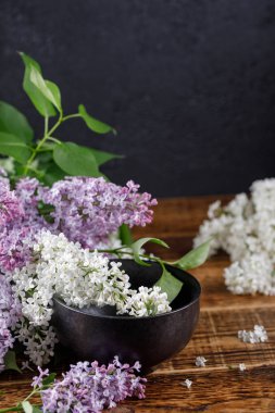Muhteşem mor ve kar-beyaz leylak çiçeklerle yakın duran siyah bir seramik kupa. Ahşap arka plan üzerinde natürmort. Yakın çekim.