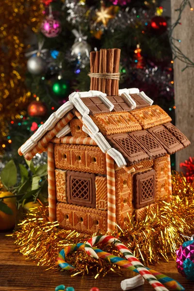 Gingerbread house decorated and Christmas sweets on the background of a dressed Christmas tree. Close-up.