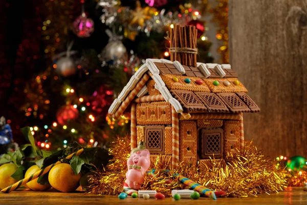 Gingerbread house and a Christmas toy pig on the background of the Christmas tree. New Year's still-life.