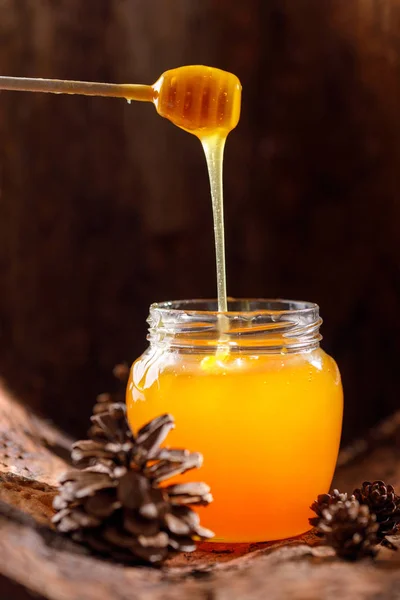 木の樹皮 コーンの背景にガラスの瓶に棒から流れる香りの蜂蜜 クローズ アップ — ストック写真