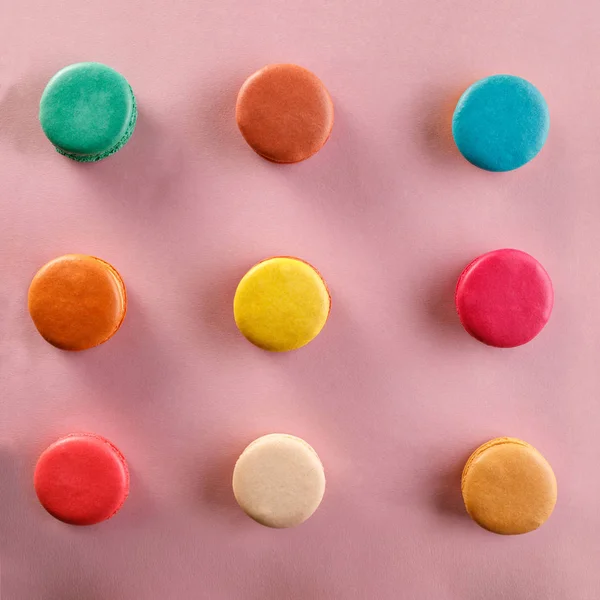 Creative layout of colorful macaroons on a pink background. Flat lay. Nutrition concept. Square.