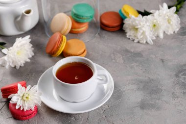 Provence kahvaltı. Parlak Fransız macarons, bir bardak çay, bir çaydanlık. Gri arka plan. Kopya alanı.