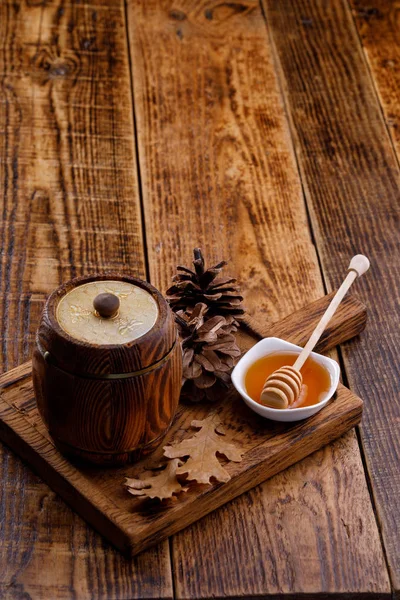 Wooden keg with honey and honey stick spoon on a decorative board. Space under the text. Close-up.