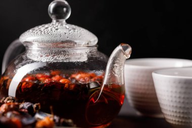 Kalça üzerinden taze demlendi vitamin içeceği ve iki kase cam çaydanlık. Kuşburnu çayı. Karanlık bir arka plan üzerinde vitamin içeceği. Yakın çekim.