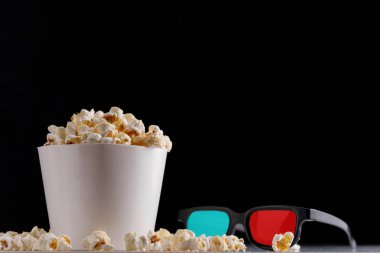 Film izlemek için çerez. Beyaz bir kova ve gözlük karanlık bir arka plan üzerinde patlamış mısır. Yakın çekim