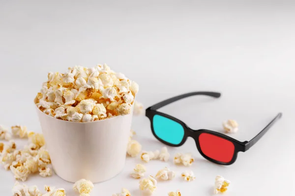 Snack to watch movies. Popcorn in a white bucket and glasses on a white background. Close-up.