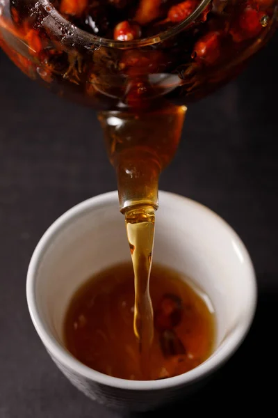 The process of brewing tea. Tea ceremony, a cup of freshly briar, a dark mood. Hot water is poured from the kettle into the cup with the hips. Close-up.