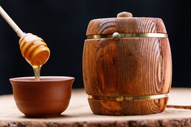 Ahşap fıçı ve bal kaşığı ayrıntılı baldan bir kase. Yakın çekim. Koyu arka plan.