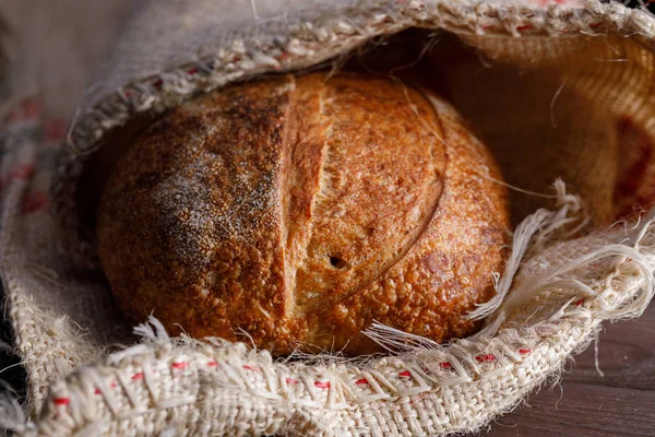 Traditional round artisan rye bread in a bag. Still life on wooden background. Close-up.