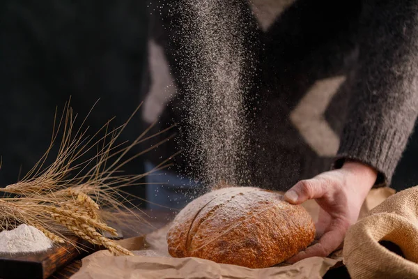 Closeup homemade bread in a man\'s hand and flour pouring. The concept of healthy food and traditional bakery. Rustic.