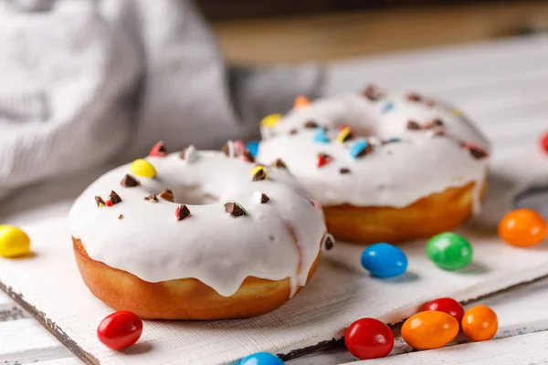 Concepção de culinária, cozimento e comida - close-up. Dois donuts em esmalte branco com cor de chocolate dragee em uma placa decorativa em um fundo escuro . — Fotografia de Stock